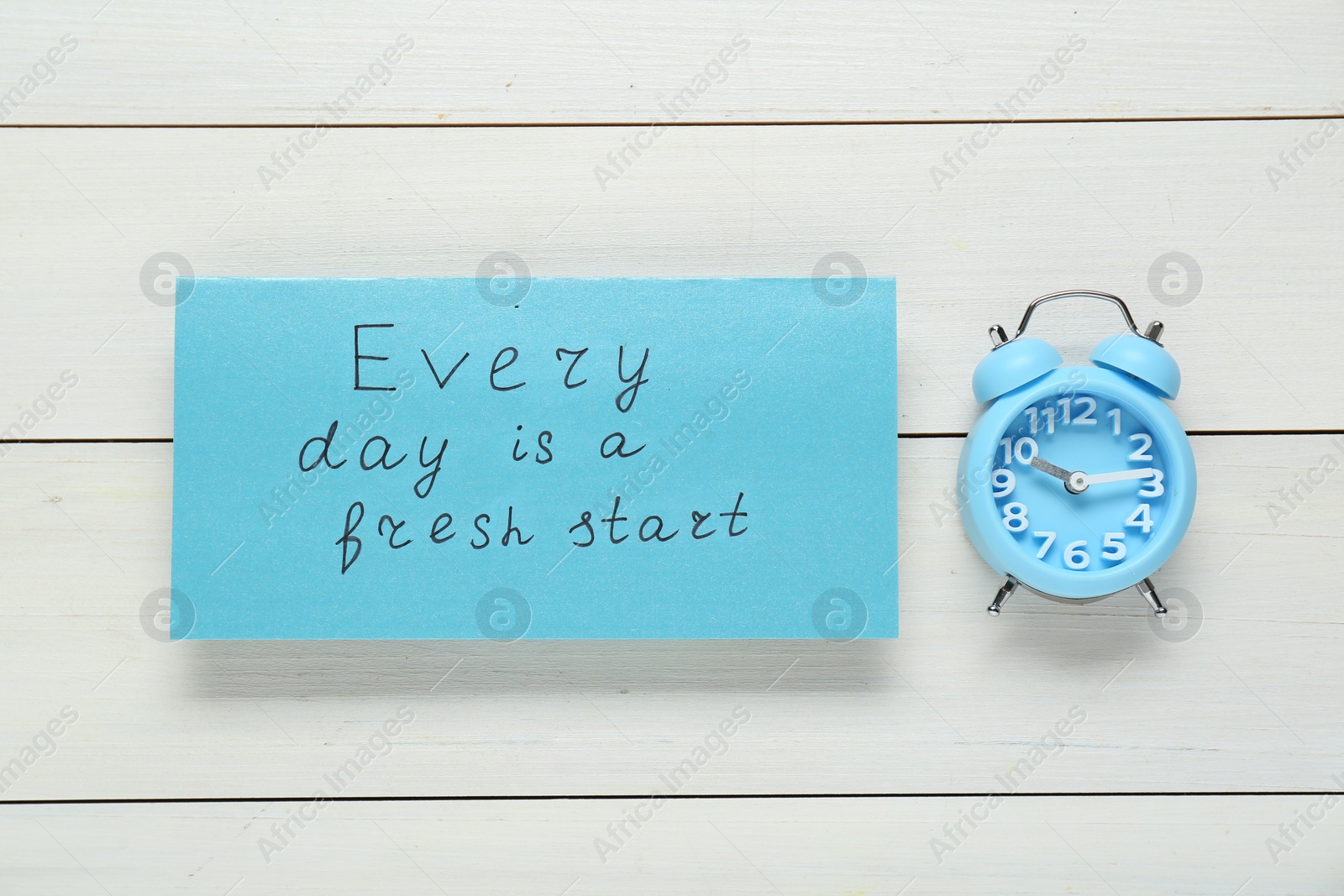 Photo of Phrase Every Day Is A Fresh Start and alarm clock on white wooden table, flat lay. Motivational quote