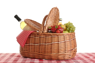 Photo of Picnic basket with wine and fruits on tablecloth against white background