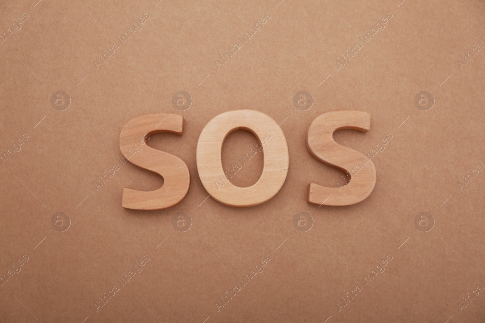 Photo of Abbreviation SOS made of wooden letters on light brown background, top view