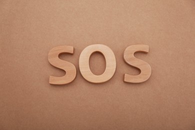 Photo of Abbreviation SOS made of wooden letters on light brown background, top view