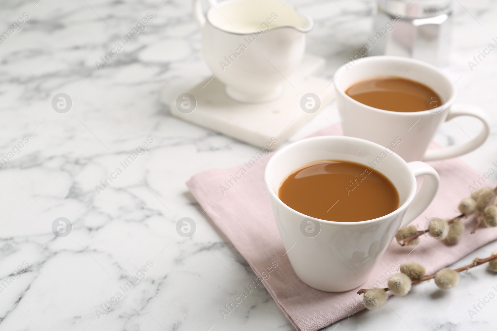 Photo of Cups of hot aromatic coffee and willow branches on white marble table. Space for text