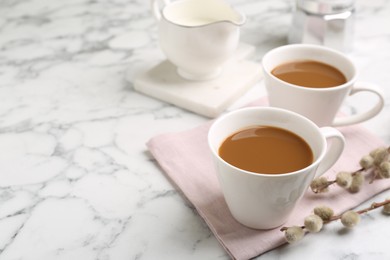 Photo of Cups of hot aromatic coffee and willow branches on white marble table. Space for text