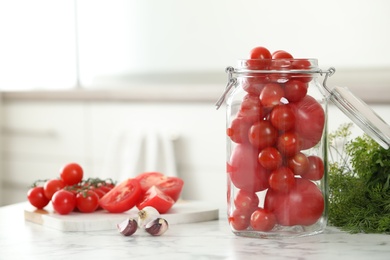Pickling jar with fresh tomatoes on white marble table in kitchen. Space for text