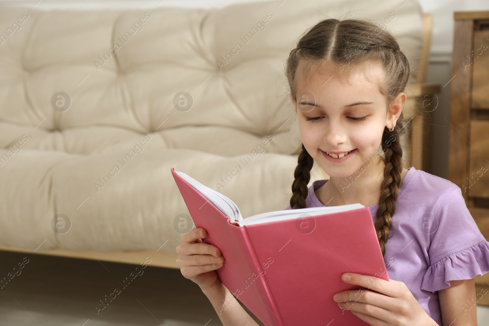 Photo of Cute little girl reading book at home. Space for text