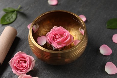 Photo of Tibetan singing bowl with water, beautiful rose flowers and mallet on gray table, closeup