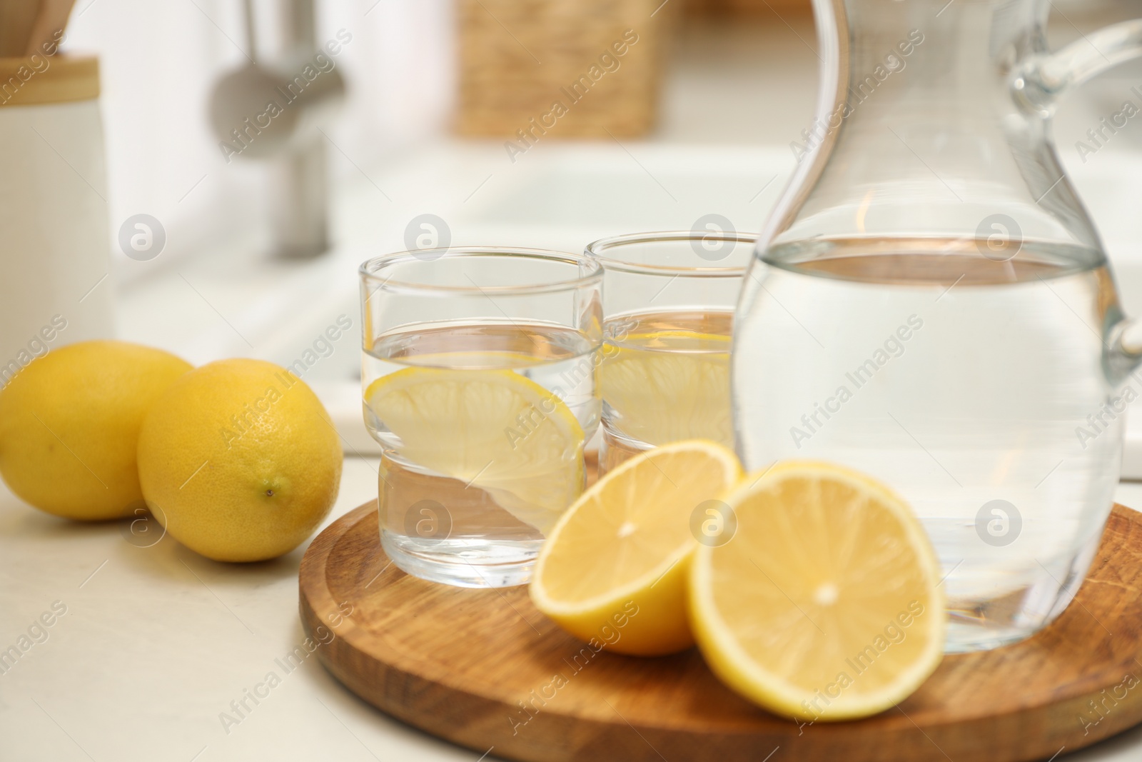 Photo of Jug, glasses with clear water and lemons on white table in kitchen, closeup
