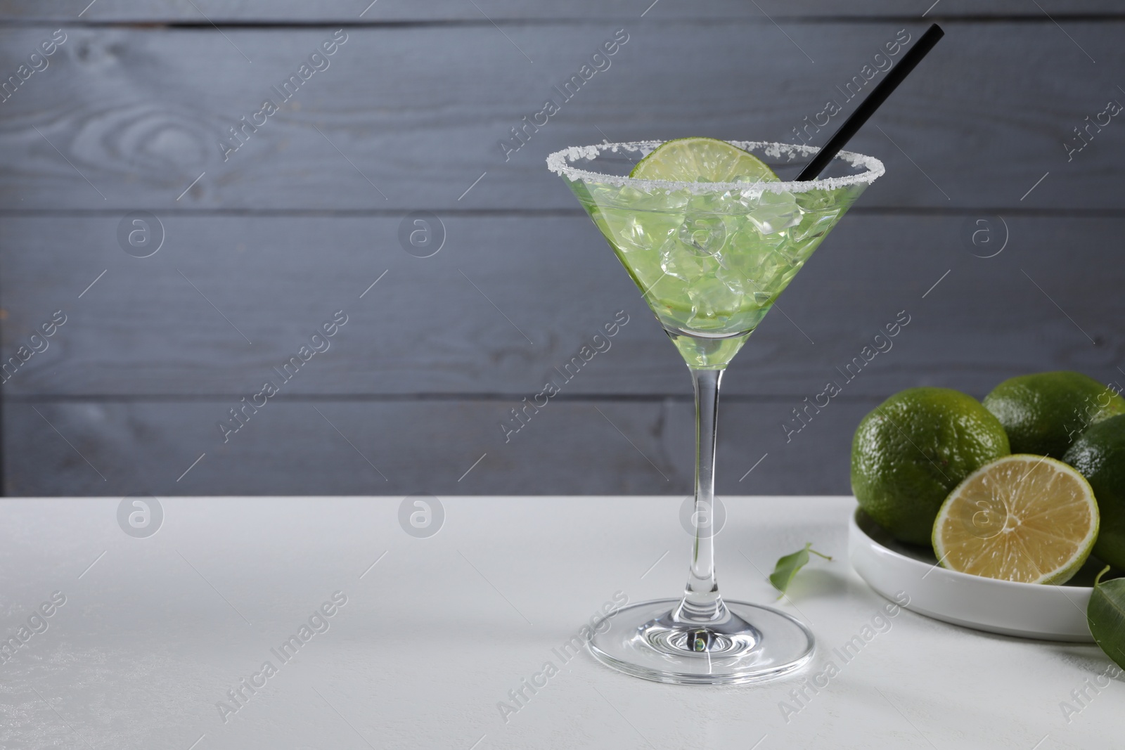 Photo of Delicious Margarita cocktail with ice cubes in glass and lime on white table, space for text