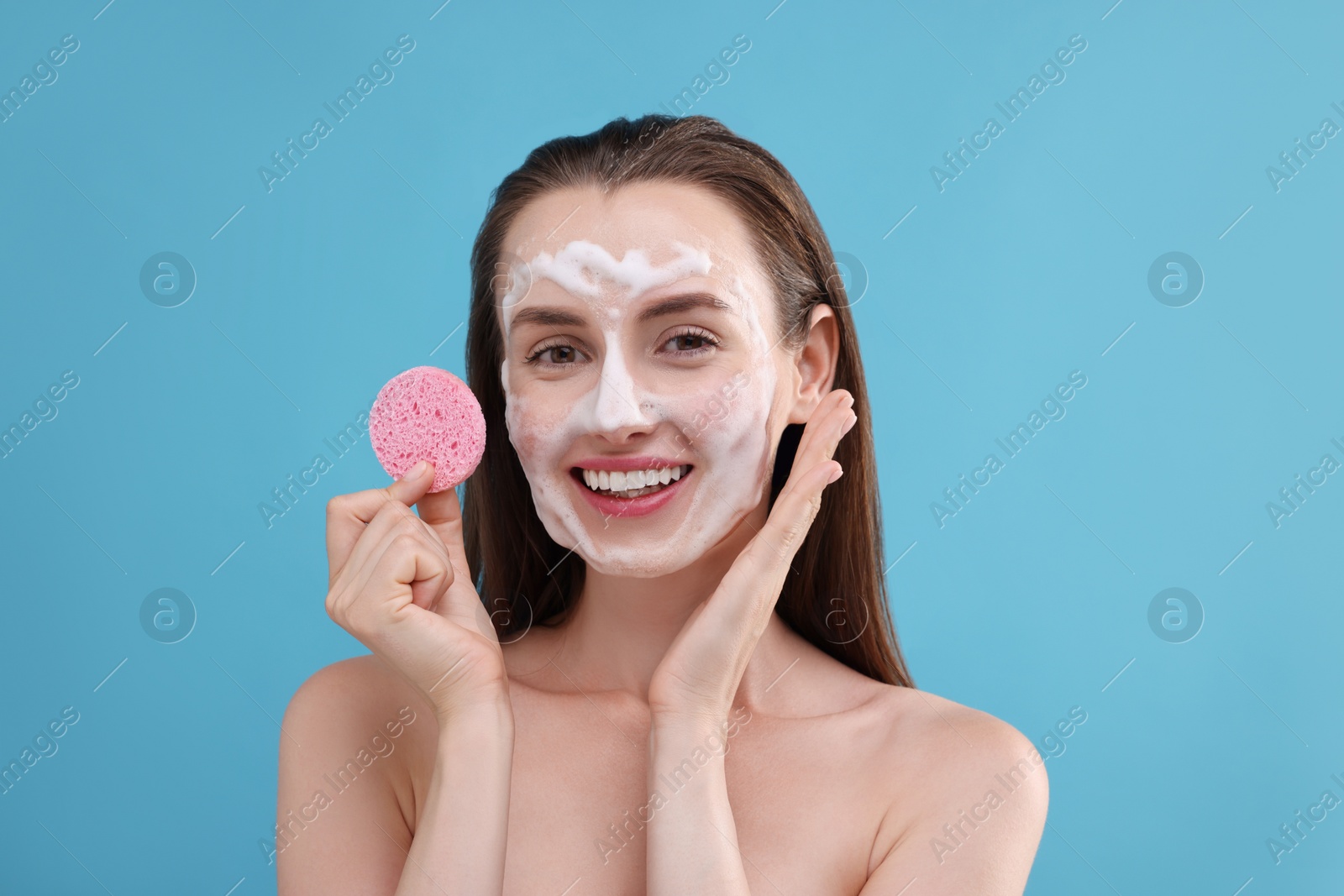 Photo of Happy young woman washing her face with sponge on light blue background