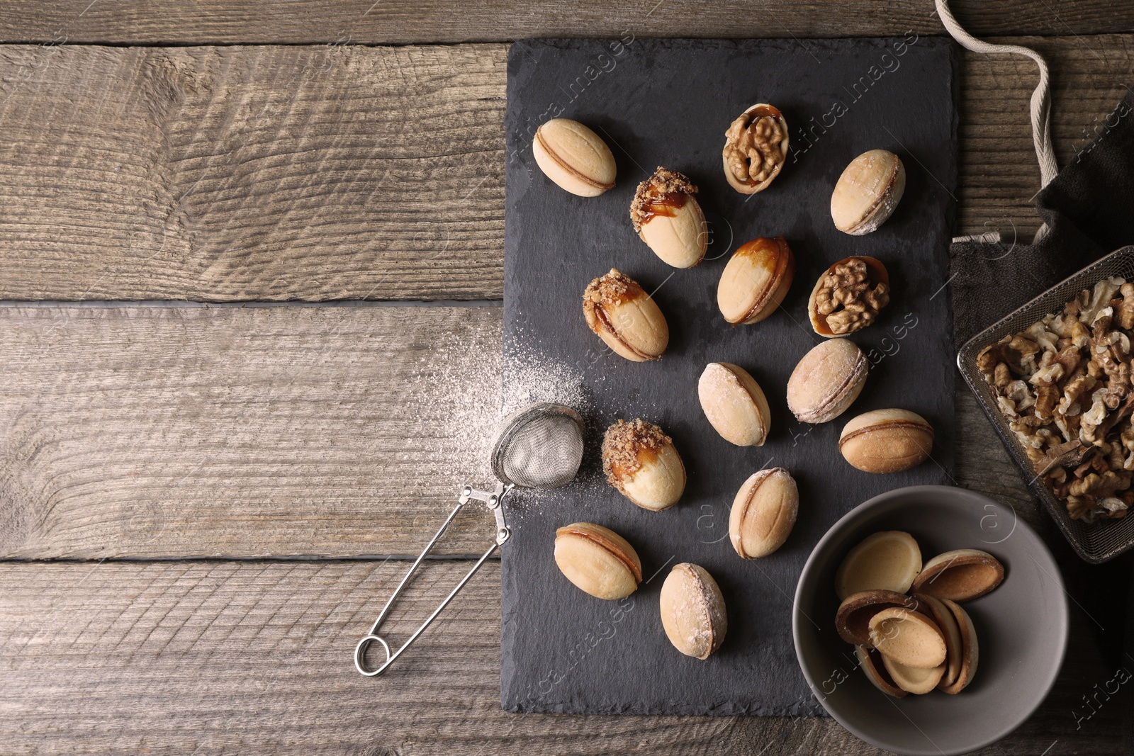 Photo of Freshly baked homemade walnut shaped cookies, nuts and flour on wooden table, flat lay. Space for text