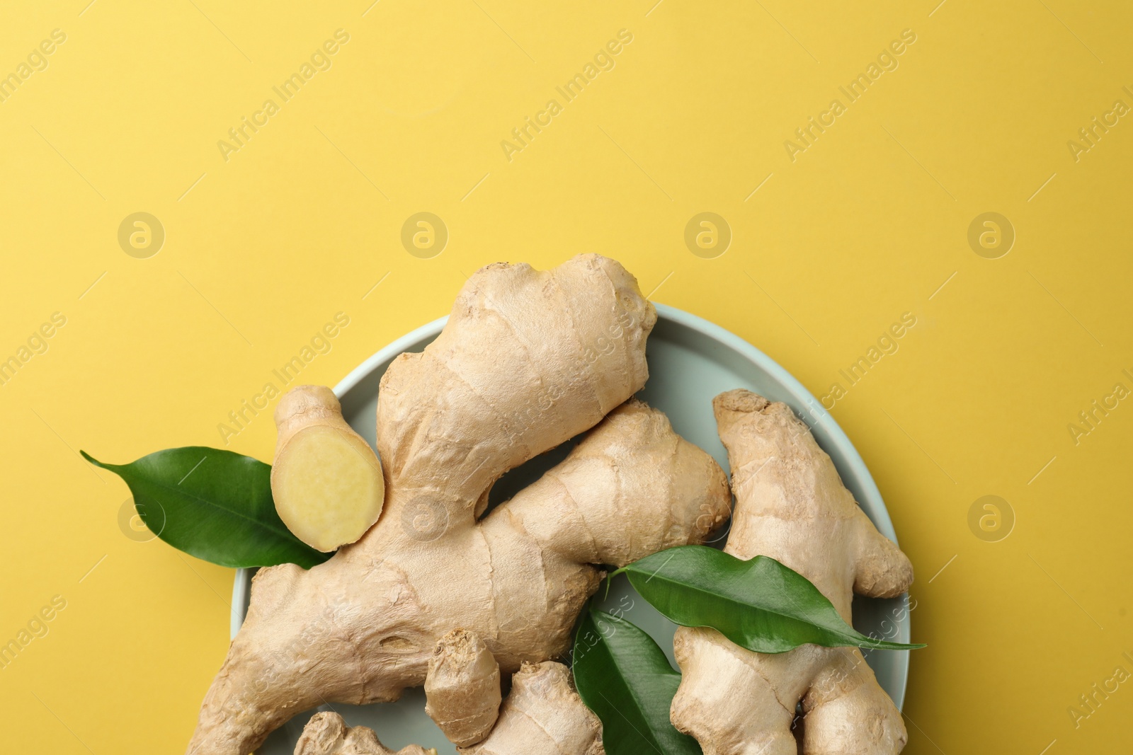 Photo of Fresh ginger with green leaves on pale light yellow background, top view. Space for text