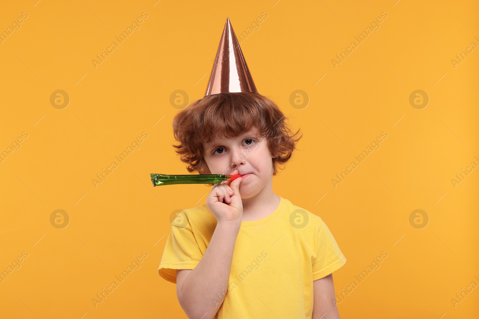 Photo of Sad little boy in party hat with blower on orange background