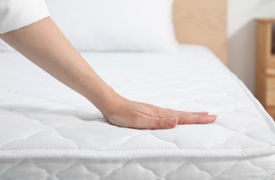 Photo of Woman touching soft white mattress on bed indoors, closeup