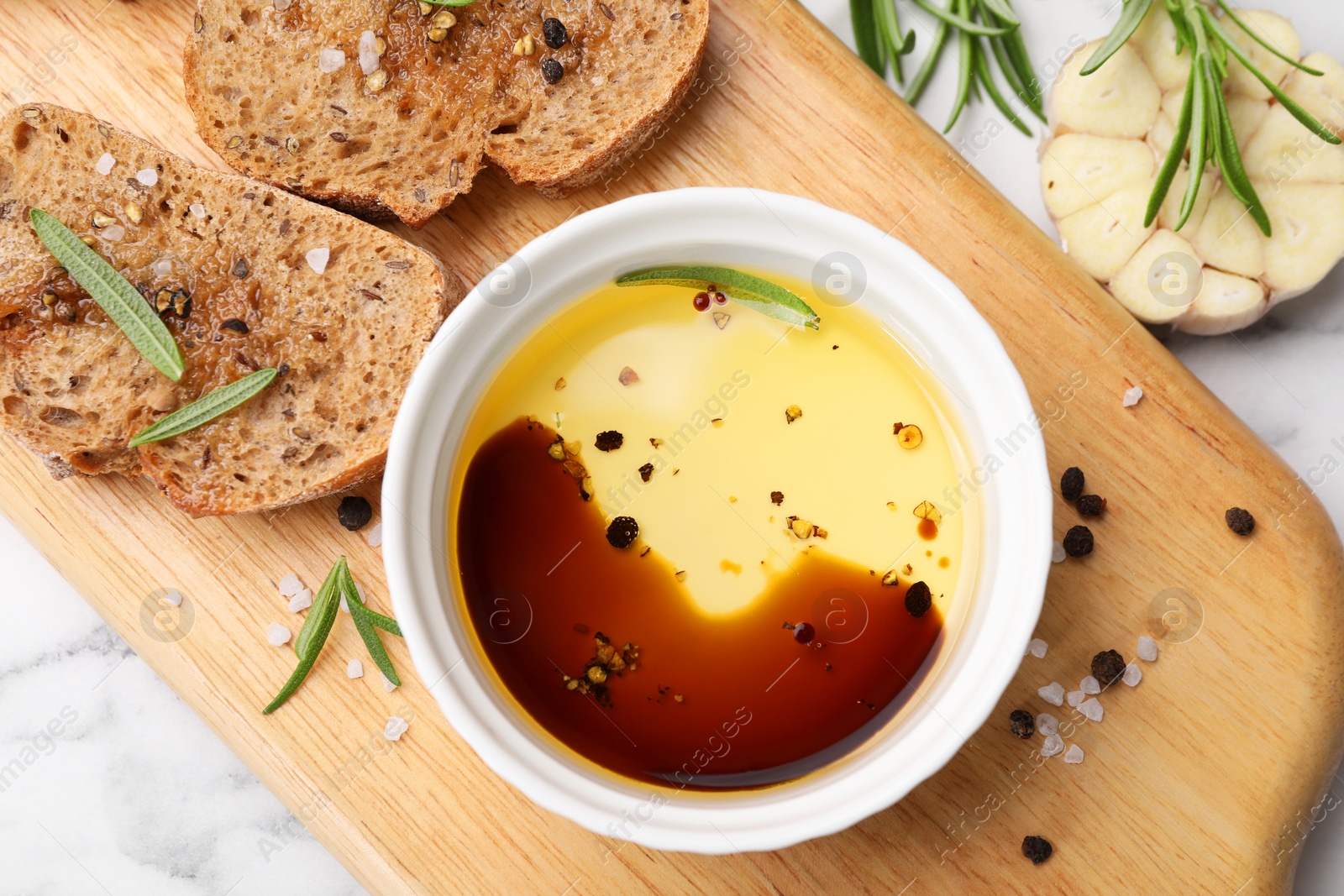 Photo of Bowl of organic balsamic vinegar with oil, bread slices and spices on white marble table, flat lay