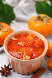 Photo of Bowl of tasty persimmon jam and ingredients on white textured table, above view