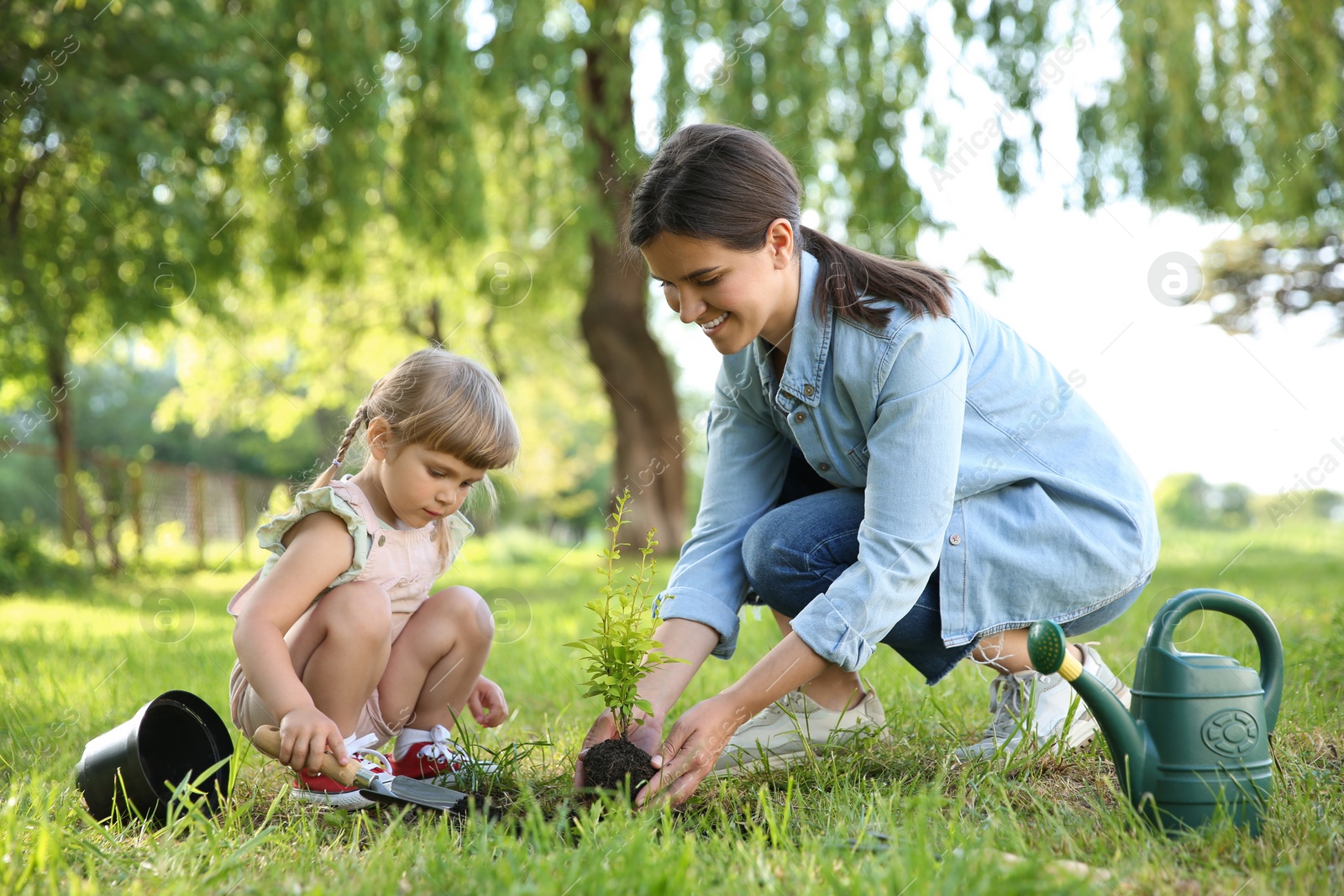 Photo of Mother and her daughter planting tree together in garden