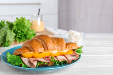 Tasty croissant sandwich with ham on white wooden table