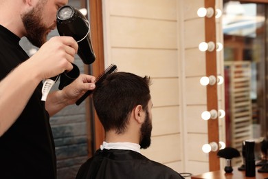 Photo of Professional hairdresser working with client in barbershop, closeup