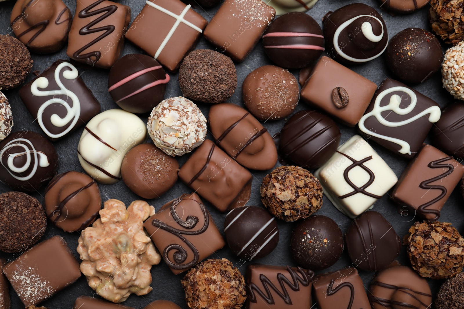 Photo of Different delicious chocolate candies on black table, flat lay