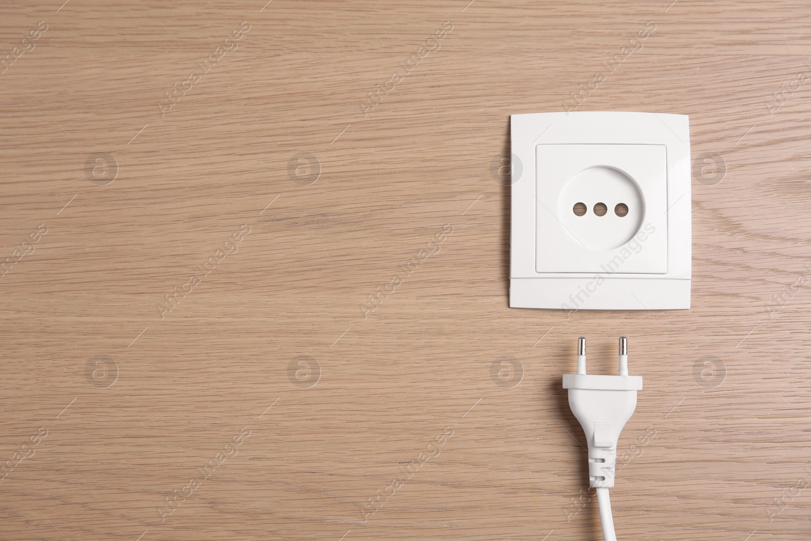 Photo of Power socket with plug on wooden table, flat lay. Space for text