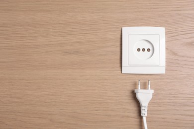 Photo of Power socket with plug on wooden table, flat lay. Space for text