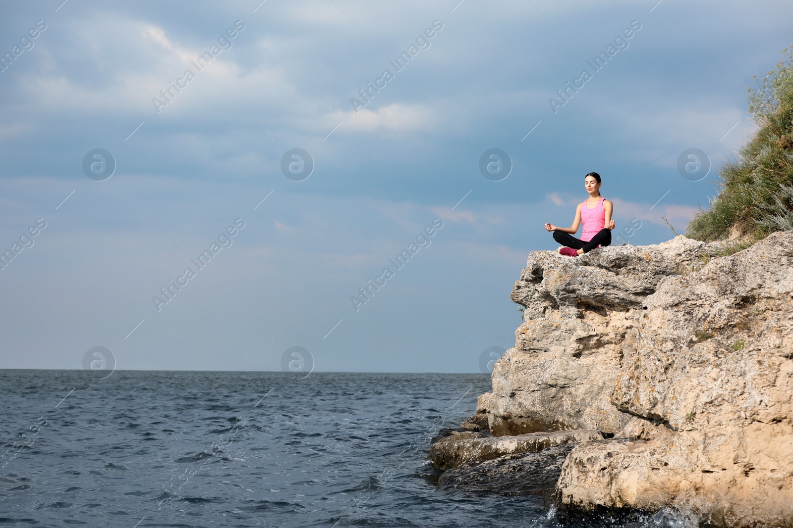 Photo of Young woman meditating on cliff near river. Space for text