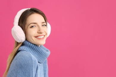 Happy woman wearing warm earmuffs on pink background, space for text