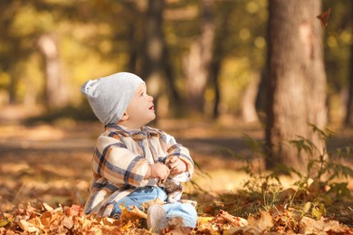 Photo of Cute little child on ground with dry leaves in autumn park, space for text