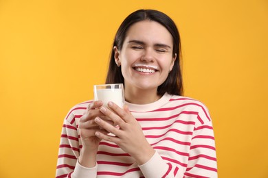 Happy woman with milk mustache holding glass of tasty dairy drink on yellow background