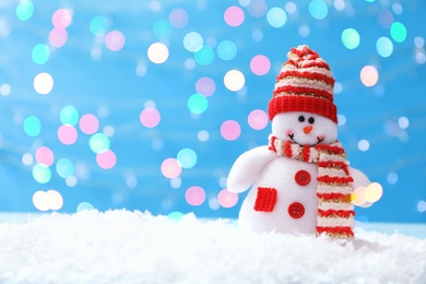 Image of Cute snowman in snow against light blue background, bokeh effect. Space for text