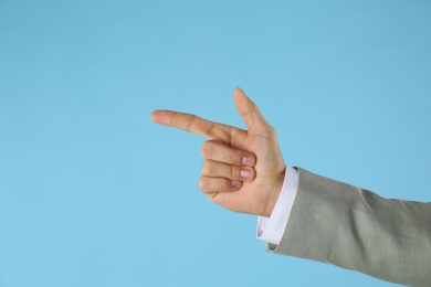 Photo of Businessman pointing at something on light blue background, closeup. Finger gesture