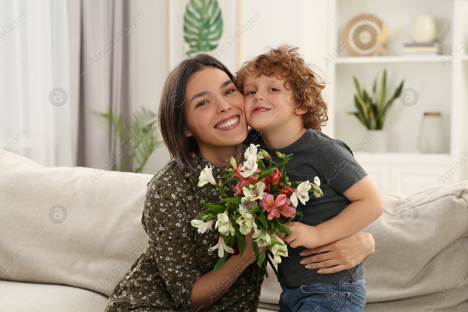 Photo of Happy woman with her cute son and bouquet of beautiful flowers at home. Mother's day celebration