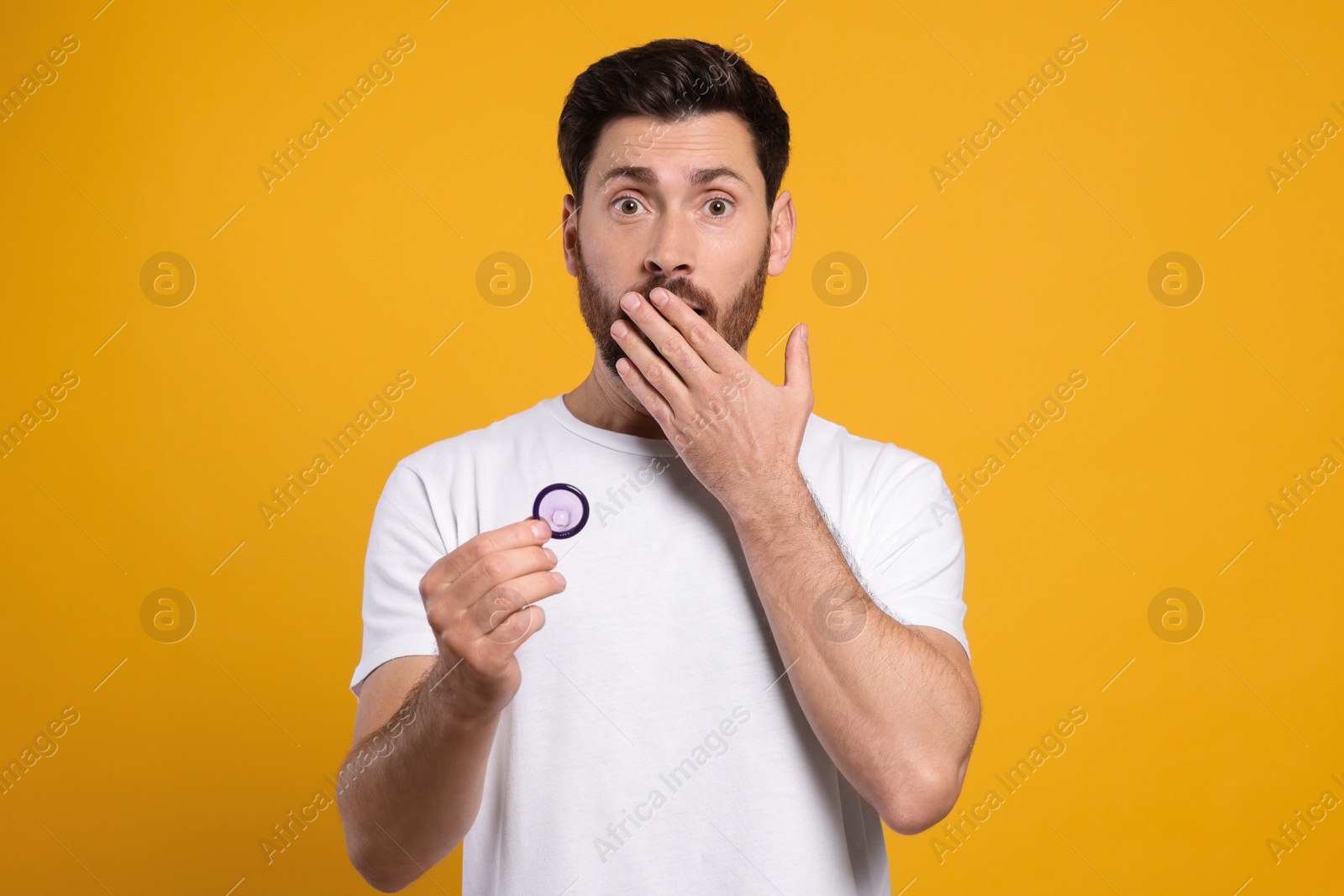 Photo of Emotional man holding condom on yellow background. Safe sex