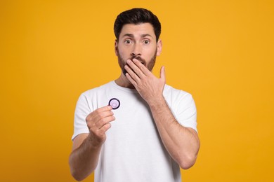 Photo of Emotional man holding condom on yellow background. Safe sex
