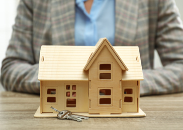 Real estate agent with house model and keys at wooden table, closeup