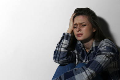 Photo of Abused young woman crying near white wall, space for text. Domestic violence concept