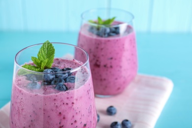 Photo of Glasses of tasty blueberry smoothie and fabric on light blue table, closeup