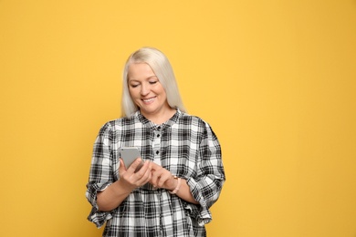 Mature woman using mobile phone on color background