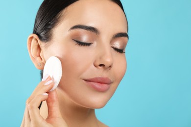Photo of Young woman using cotton pad with micellar water on light blue background, closeup