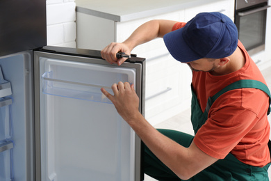 Male technician with pliers repairing refrigerator indoors