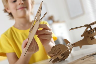 Photo of Little boy making carton toys at table indoors, closeup. Creative hobby