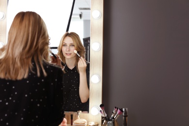 Young woman applying makeup near mirror in dressing room