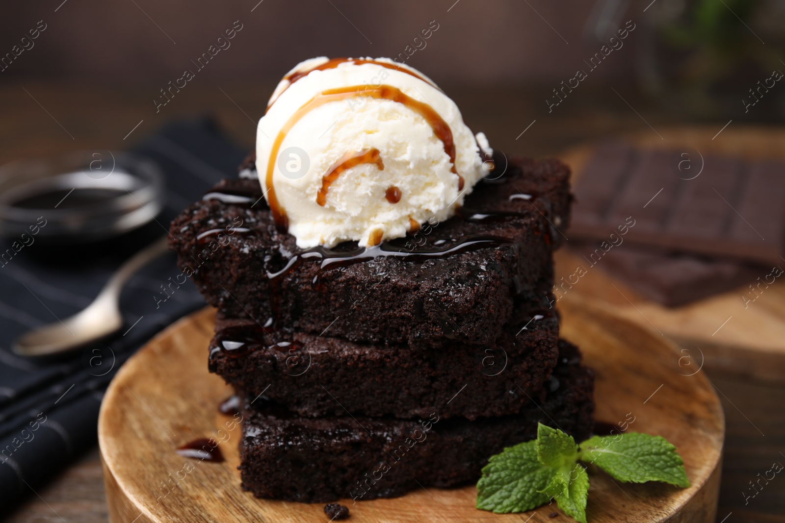 Photo of Tasty brownies served with ice cream and caramel sauce on table, closeup