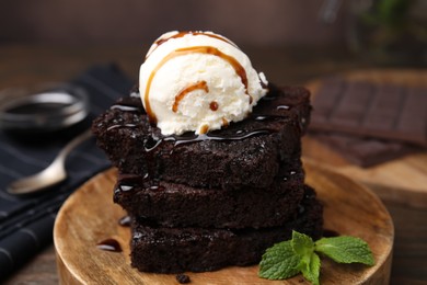 Photo of Tasty brownies served with ice cream and caramel sauce on table, closeup