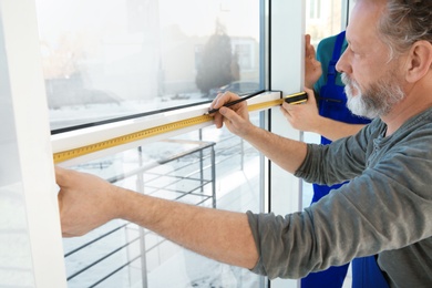 Service men measuring window for installation indoors