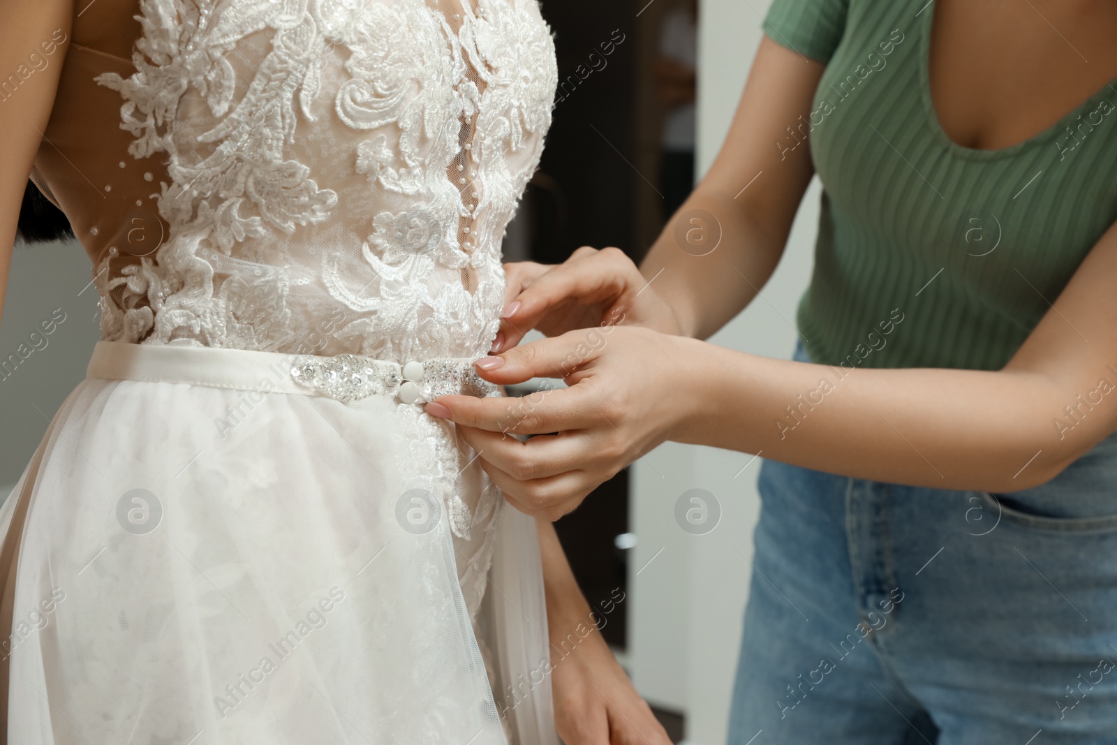 Photo of Woman helping bride wear wedding dress in boutique, closeup