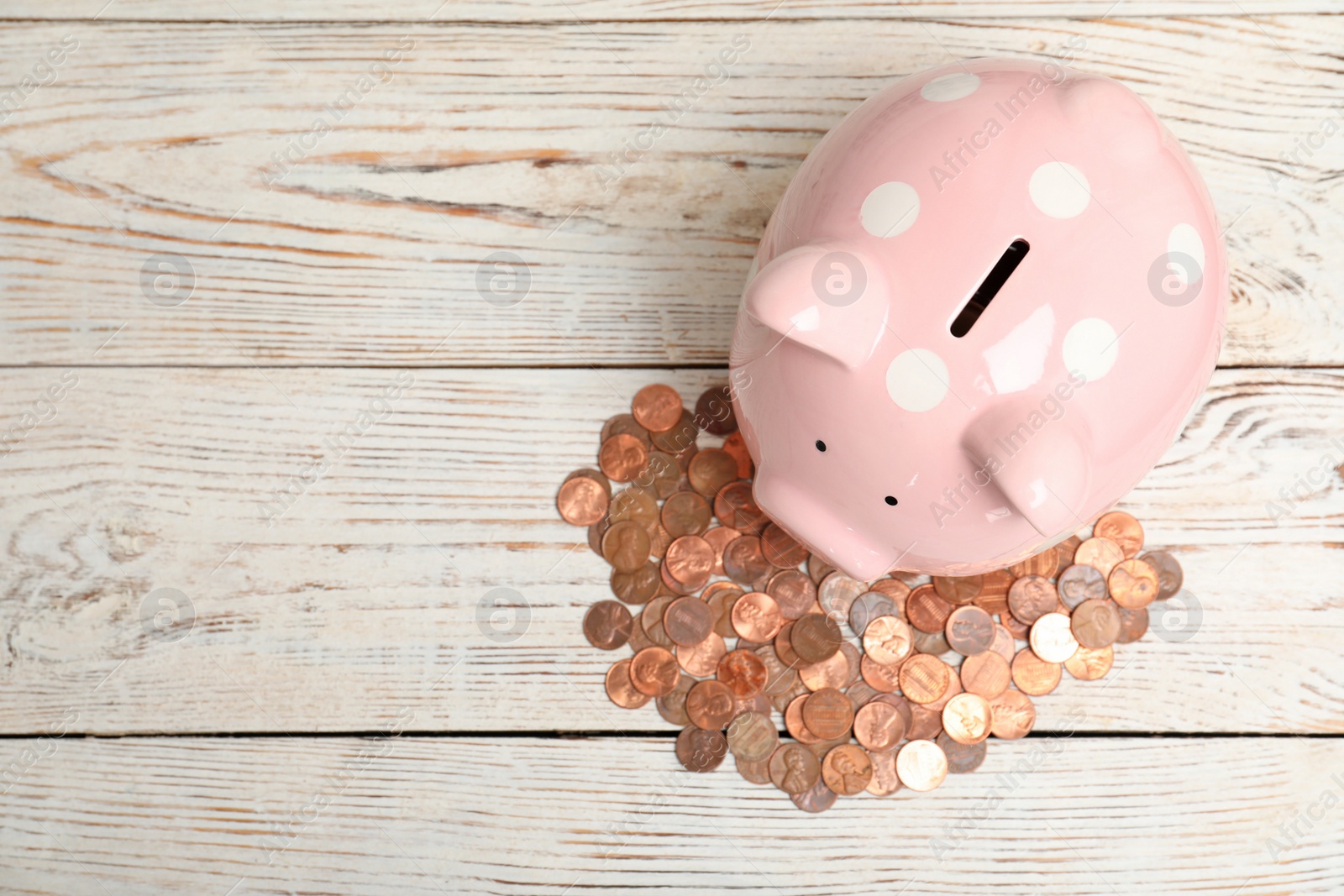 Photo of Ceramic piggy bank, many coins and space for text on white wooden background, top view