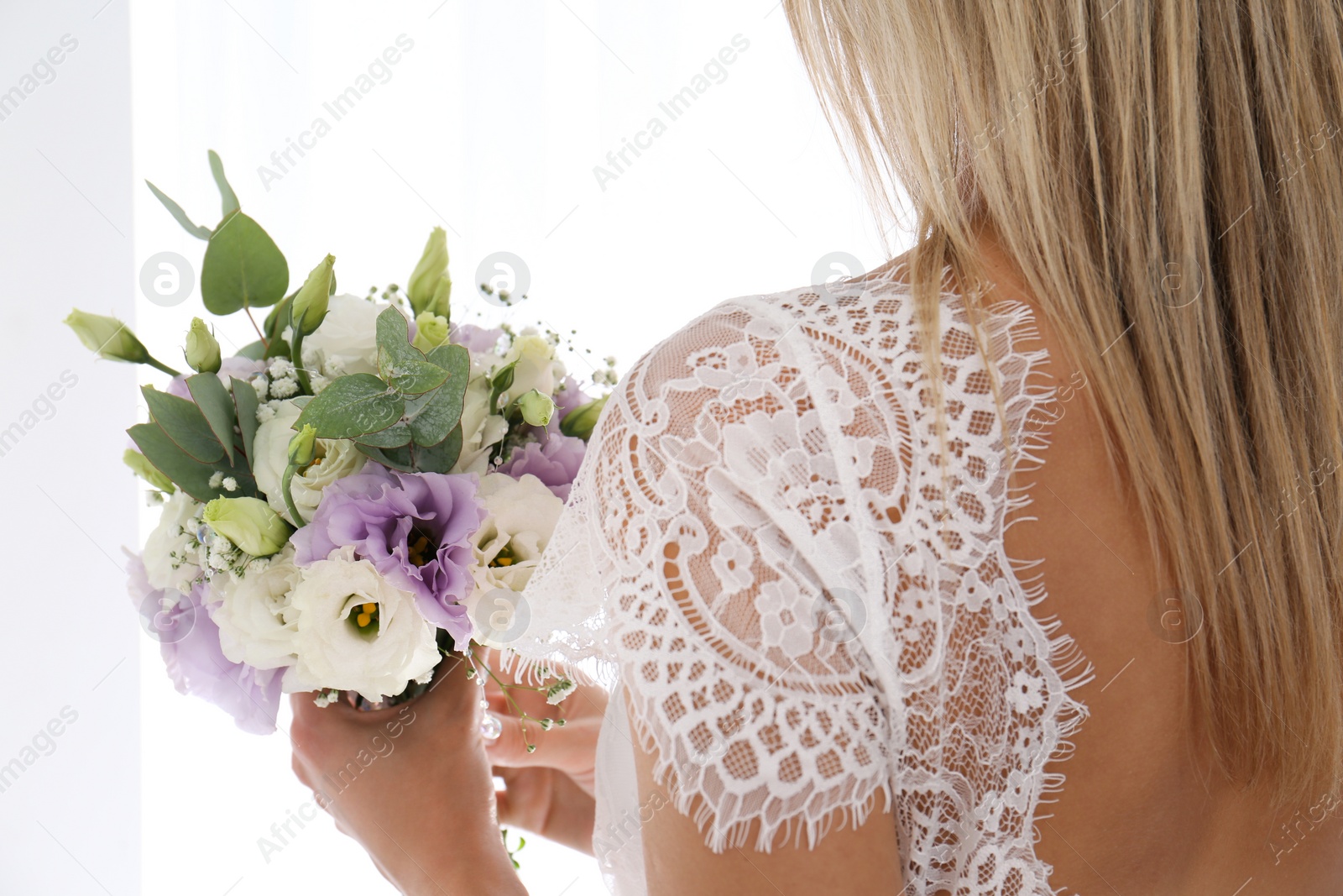 Photo of Bride holding beautiful bouquet with Eustoma flowers indoors, closeup