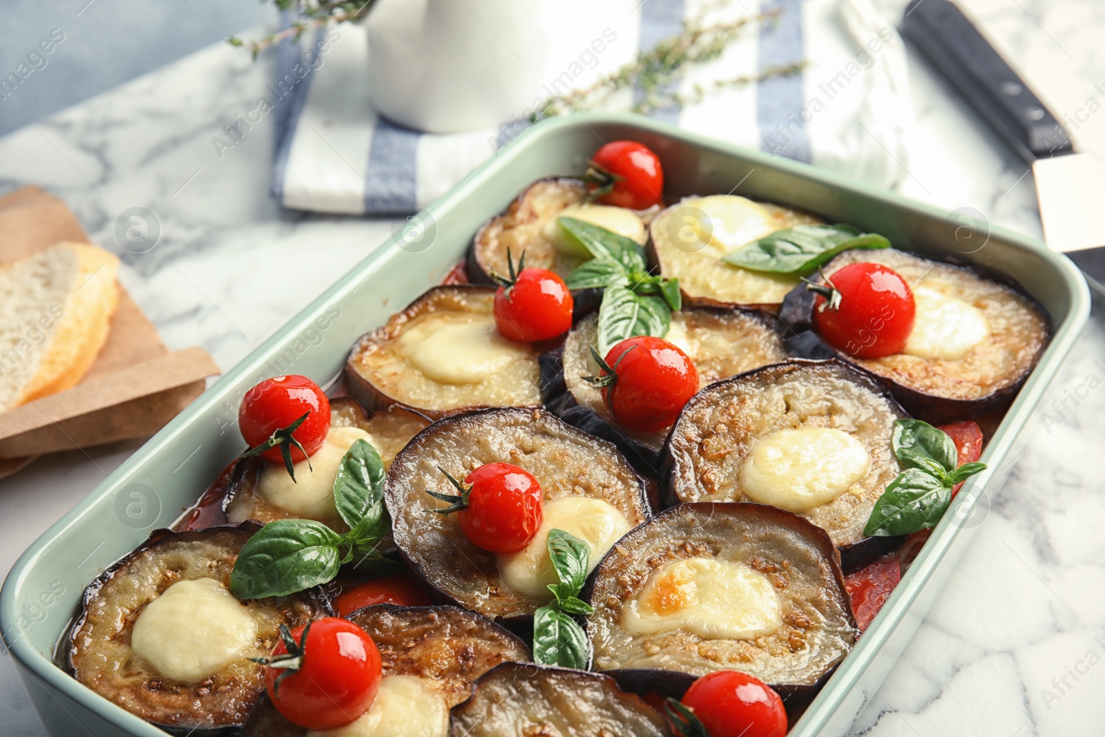 Photo of Baked eggplant with tomatoes, cheese and basil in dishware on marble table, closeup