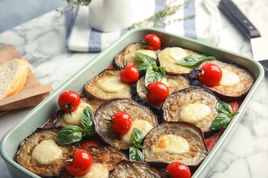 Photo of Baked eggplant with tomatoes, cheese and basil in dishware on marble table, closeup