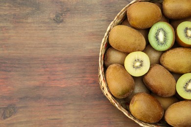 Photo of Basket of many whole and cut fresh kiwis on wooden table, top view. Space for text